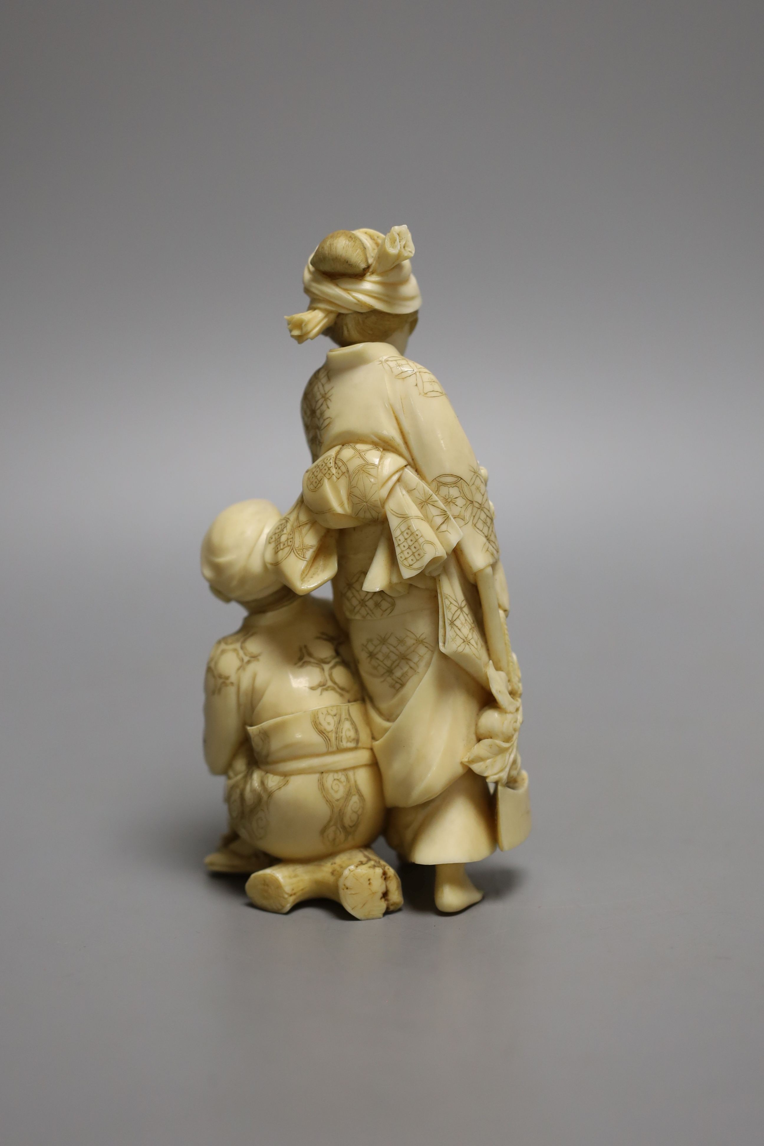 A Japanese ivory okimono of a crouching man and a woman holding a flower basket, Meiji period, signed - 15cm tall